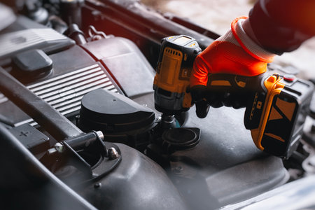 Close-up of a mechanic using a cordless drill while repairing a car engine. Concept of car maintenance and mechanical works in garageの写真素材
