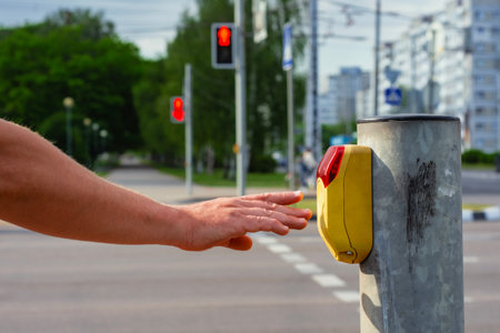 Man presses a yellow crosswalk button against a traffic light on a city street with a traffic light with a burning red light. Pedestrian safety concept.の写真素材