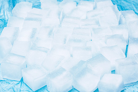 Frozen ice cubes for drinks arranged in a scattered pattern on a blue surfaceの写真素材