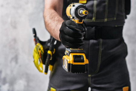 Uniformed construction worker holding a yellow colored cordless screwdriver with a set of tools on his belt. The concept of repair, maintenance and electrical installationの写真素材