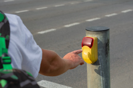 Man presses a yellow crosswalk button against a traffic light on a city street with a traffic light with a burning red light. Pedestrian safety concept.の写真素材