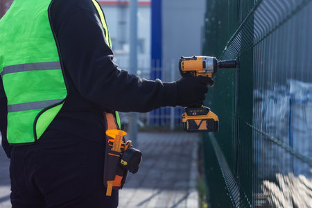 A worker in a green safety vest uses a yellow impact drill at a construction site. Safety concept for workers in the construction industryの写真素材