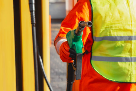 Gas station worker in signal clothing holding a gasoline gun at a fueling station. Fueling station concept on the theme of transportation and energy resourcesの写真素材