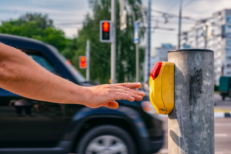 Man presses a yellow crosswalk button against a traffic light on a city street with a traffic light with a burning red light. Pedestrian safety concept.の写真素材