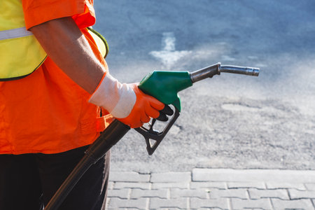 Gas station worker in signal clothing holding a gasoline gun at a fueling station. Fueling station concept on the theme of transportation and energy resourcesの写真素材