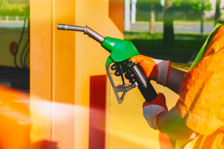 Gas station worker in signal clothing holding a gasoline gun at a fueling station. Fueling station concept on the theme of transportation and energy resourcesの写真素材
