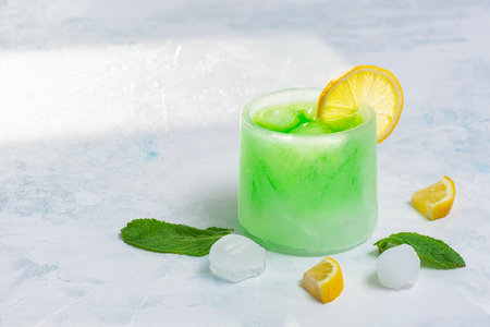 Green cocktail in an ice glass garnished with lemon slice, mint leaves, lemon slices and ice cubes. The concept emphasizes the coolness, freshness and creative presentation of summer fruit drinksの写真素材