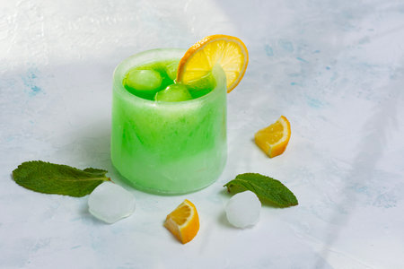 Green cocktail in an ice glass garnished with lemon slice, mint leaves, lemon slices and ice cubes. The concept emphasizes the coolness, freshness and creative presentation of summer fruit drinksの写真素材