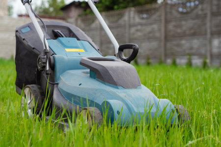 Closeup of blue electric lawn mower cutting fresh green grass. A moment of lawn care, emphasizing the care of the yard and garden toolsの写真素材