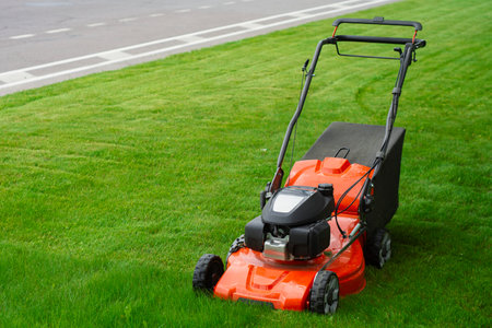 Bright orange lawn mower on lush green grass. Concept garden care, landscaping and summer outdoor work. Garden tool for lawn care and country lifestyleの写真素材
