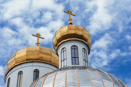 Golden onion domes of an Orthodox church under a blue sky with clouds. Architecture with white walls and gilded crosses. Religious traditions and design of the church in Russian styleの写真素材