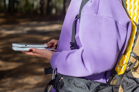 Close-up a woman with a hiking backpack and a smartphone and portable power bank in hands, against the background of a tent in the forest. Digital nomad's concept of sustainable existence in natureの写真素材
