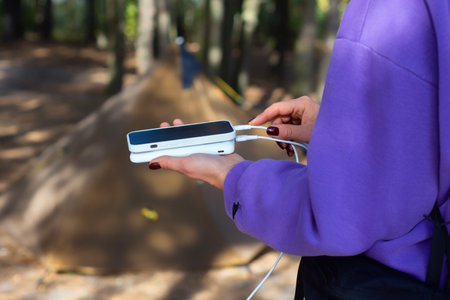 Close-up of a woman with smartphone and portable power bank in hands, against the background of a tent in the forest. Digital nomad's concept of sustainable existence in natureの写真素材