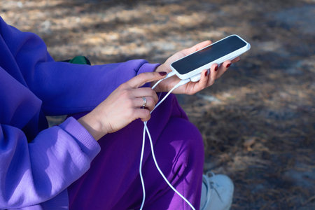 Woman close-up with smartphone and portable power bank in hands on forest background. The concept of sustainable existence of a digital nomad in natureの写真素材