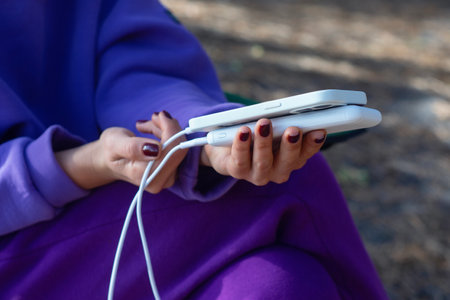 Woman close-up with smartphone and portable power bank in hands on forest background. The concept of sustainable existence of a digital nomad in natureの写真素材