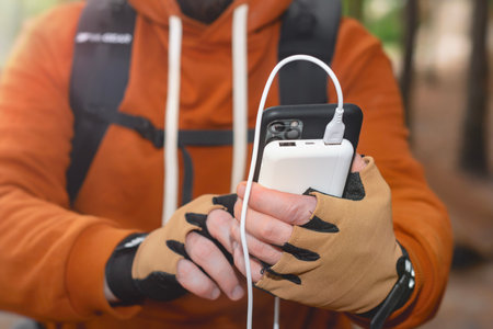 Close-up of a man with a hiking backpack, smartphone and portable power bank in his hands, in the background in the forest. The concept of sustainable existence of a digital nomad in natureの写真素材