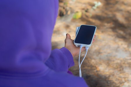 Woman close-up with smartphone and portable power bank in hands on forest background. The concept of sustainable existence of a digital nomad in natureの写真素材