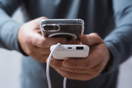 Close-up of a man holding a power bank and charging a smartphone. Portable charger for phone and gadgetsの写真素材