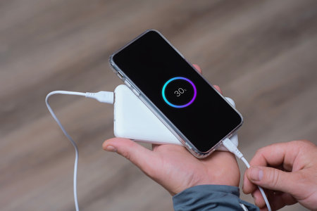 Close-up of a man holding a power bank and charging a smartphone. Portable charger for phone and gadgetsの写真素材
