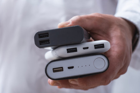 Man hand holds three different power banks. Modern portable chargers with USB connectors for charging smartphones and gadgetsの写真素材