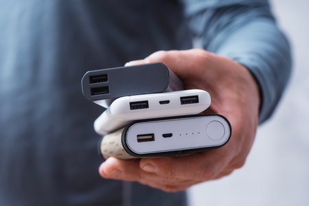 Man hand holds three different power banks. Modern portable chargers with USB connectors for charging smartphones and gadgetsの写真素材