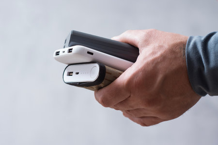 Man hand holds three different power banks. Modern portable chargers with USB connectors for charging smartphones and gadgetsの写真素材