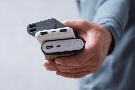 Man hand holds three different power banks. Modern portable chargers with USB connectors for charging smartphones and gadgetsの写真素材