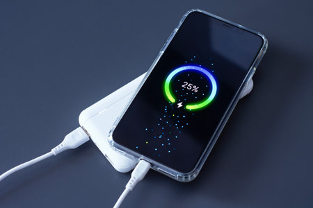 Power Bank charges your smartphone via USB cable on dark background. Portable charger for phones and gadgetsの写真素材