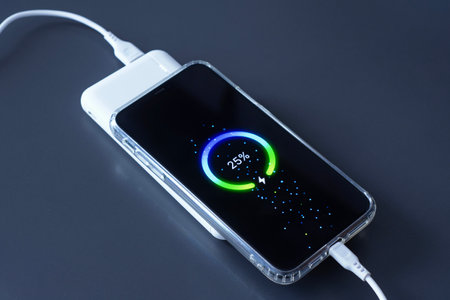 Power Bank charges your smartphone via USB cable on dark background. Portable charger for phones and gadgetsの写真素材