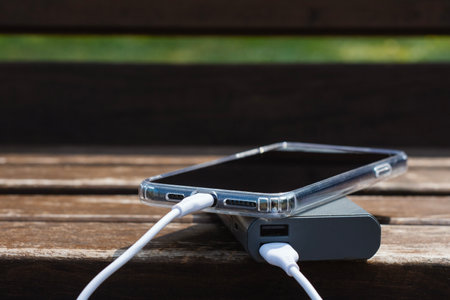 Smartphone charging from Power Bank on rustic wooden bench. The concept of technology on the go, modern living and vacationing in natureの写真素材