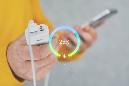 Close-up of hands holding a Smartphone connected to a portable Power Bank, with a glowing digital battery indicator showing the percentage of charge.の写真素材