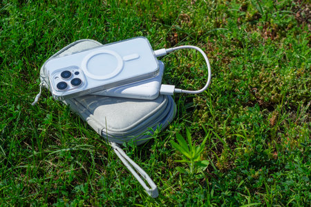 Smartphone connected to a Power Bank lies on the grass in a small bag. Outdoor charging concept, portable energy while traveling in natureの写真素材