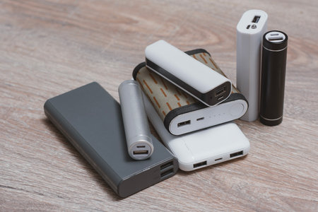 Assortment of portable power banks in various designs on a wooden surface. Portable chargers for gadgetsの写真素材