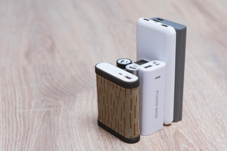 Assortment of portable power banks in various designs on a wooden surface. Portable chargers for gadgetsの写真素材