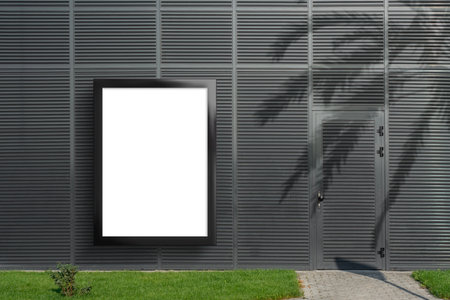 Realistic mockup of a vertical billboard with a black frame, located on a ribbed gray wall of a building. Poster for displaying street advertisements and postersの写真素材