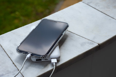 Close up of smartphone in transparent case connected to white portable charger discussed on light marble surfaceの写真素材