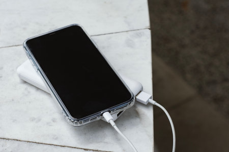 Close up of smartphone in transparent case connected to white portable charger discussed on light marble surfaceの写真素材