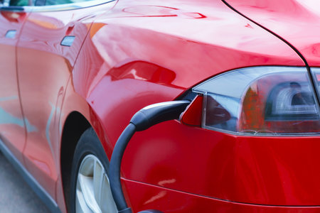 Close-up of an electric charger connected to a red electric vehicle. Clean energy concept and the transition to green transportationの写真素材
