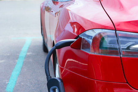 Close-up of an electric charger connected to a red electric vehicle. Clean energy concept and the transition to green transportationの写真素材