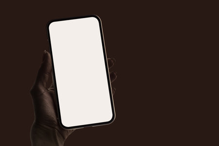 Woman hand holding mockup Smartphone with a blank white screen isolated on brown background. Concept for showcasing mobile app interfaces and web designsの写真素材