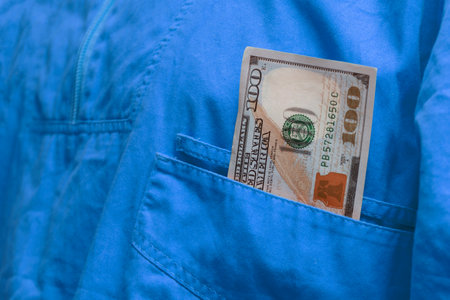 Crisp one hundred dollar bill sticking out of the pocket of an blue jumpsuit. Concept related to corruption, bribery and crimeの写真素材