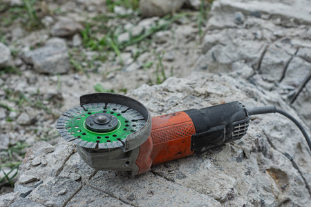 Close-up of an angle grinder with a green segmented diamond cutting disc placed on rough concrete paving stonesの写真素材