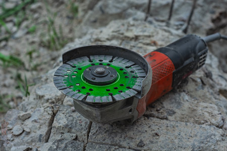 Close-up of an angle grinder with a green segmented diamond cutting disc placed on rough concrete paving stonesの写真素材