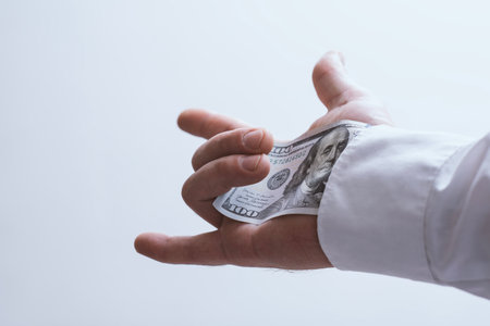 Close-up of a male hand pulling a dollar bill from the sleeve of a white shirt. Symbol of corruption, bribery, hidden transactions and secret paymentの写真素材