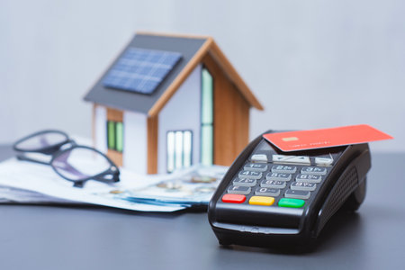 Payment terminal for credit card payment, US dollars and solar powered house model. Concept of property payment and real estate transactions for green housingの写真素材
