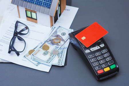 Payment terminal for credit card payment, US dollars and solar powered house model. Concept of property payment and real estate transactions for green housingの写真素材