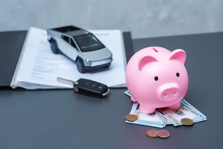 Pink piggy bank on a US dollar bills with coins, car key and electric vehicle on contract papers. Concept for saving money for buying an electric car, car loan, financial planningの写真素材