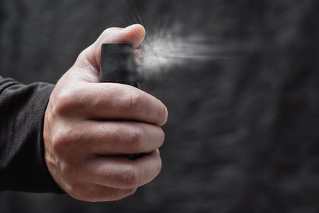 Close-up of a man hand pressing a pepper spray canister with visible aerosol release. Concept self-defense, protection, danger prevention, and personal safetyの写真素材