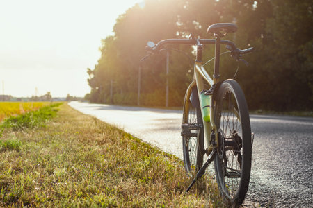 Road bike parked on the side of a rural road at sunset. Sunshine, green fields and peaceful atmosphere speak of freedom, traveling and healthy lifestyleの写真素材