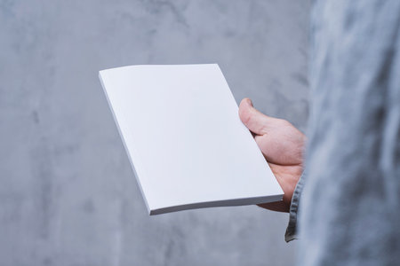 Realistic mockup of book cover, magazine in the hands of a man on concrete background. Concept for demonstrating editorial design, book covers and printed materialsの写真素材